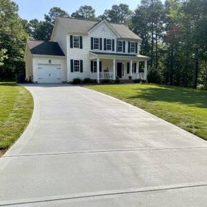 Newly installed concrete driveway leading to a two-story house in Greensboro, NC, showcasing durability and aesthetic appeal, surrounded by a well-maintained lawn.