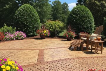 Beautiful stamped concrete patio in a North Carolina backyard, featuring decorative landscaping, colorful flower pots, and an inviting wooden lounge chair.